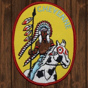 May include: A yellow and red embroidered patch with a Native American warrior riding a white horse. The patch is oval shaped and has the word "CHEYENNE" written around the edge.