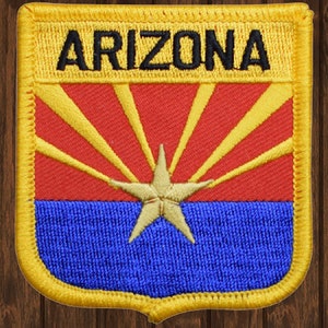 May include: A yellow embroidered patch with the word "ARIZONA" in black lettering. The patch features the Arizona state flag with a red background, a yellow star, and yellow rays emanating from the star.