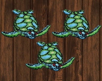 May include: Three green and blue embroidered sea turtle patches. The turtles have red eyes and are swimming.