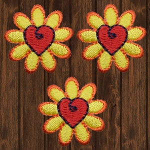 May include: Three yellow flower-shaped fabric patches with red hearts in the centre. The hearts have a black outline. The flowers have orange outlines.
