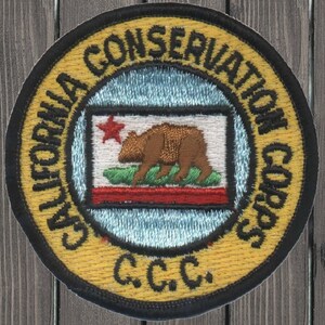 May include: A yellow and black round patch with the text "California Conservation Corps" and "C.C.C."  The patch features a stylized image of the California state flag with a bear and a red star.