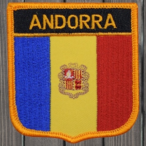 Puede incluir: Un parche bordado con los colores de la bandera de Andorra, amarillo, azul y rojo, con la palabra "ANDORRA" en letras amarillas sobre fondo negro. El parche está rodeado por un borde amarillo.