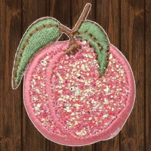 May include: A pink peach with green leaves, covered in glitter, is embroidered on a fabric patch.