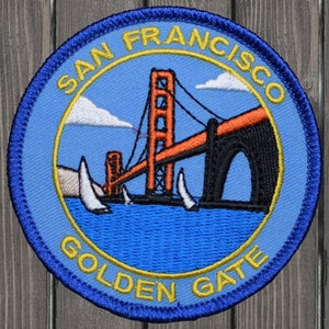 May include: Embroidered patch depicting the Golden Gate Bridge in San Francisco. The design shows the bridge in orange, blue water, white sailboats, and the text "SAN FRANCISCO GOLDEN GATE" in yellow, within a blue circular border.