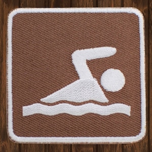May include: A brown fabric patch with a white embroidered swimming icon. The icon depicts a person swimming with their arms outstretched and head above the water.