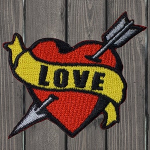 Op de afbeelding: Een rood hart met een pijl erdoorheen en een geel spandoek met de tekst "LOVE" erop. Het hart is geborduurd met een textuur.