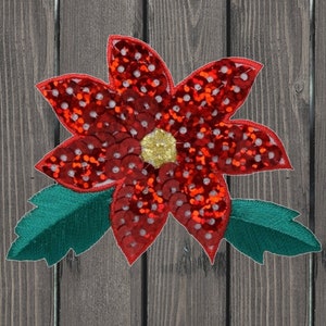 May include: A red poinsettia flower with green leaves, made of sequins and embroidery. The flower is a popular Christmas decoration.