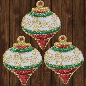 May include: Three white Christmas ornaments with red, green, and gold trim. The ornaments are decorated with gold swirls.