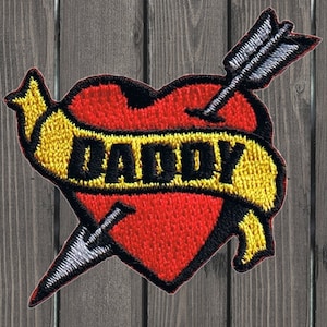 May include: Red heart with an arrow through it and a yellow banner that says "Daddy".