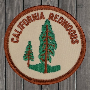 May include: A brown and white embroidered patch with the text "CALIFORNIA REDWOODS" in brown lettering. The patch features two green trees with brown trunks.
