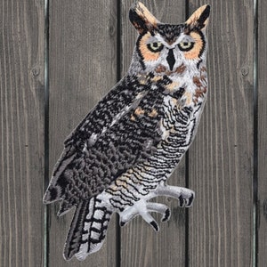 May include: Embroidered iron-on patch of a brown and gray owl with yellow eyes. The owl is perched on a branch with its wings spread out.