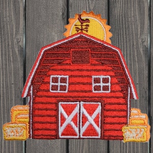 May include: Red barn with white windows and a white X-shaped door. The barn has a yellow sun with a red bird on top. There are yellow hay bales on either side of the barn.