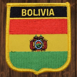 May include: A yellow, red, and green embroidered patch with the word "BOLIVIA" in yellow lettering on a black background. The patch features the coat of arms of Bolivia in the center.