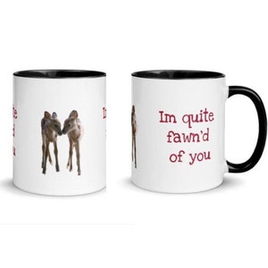 Puede incluir: Taza de café de cerámica blanca con borde negro. La taza tiene una imagen roja de dos cervatillos en el lado izquierdo y el texto "I'm quite fawn'd of you" en el lado derecho.