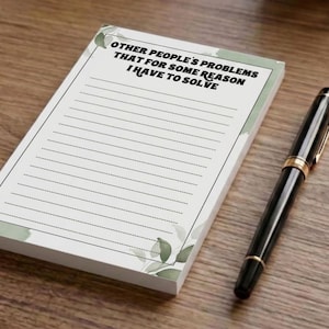 May include: A rectangular notepad with a white background and green leaf accents at the corners. The top features the text OTHER PEOPLE'S PROBLEMS THAT FOR SOME REASON I HAVE TO SOLVE above a series of horizontal lines for writing. A black pen.