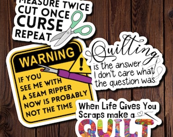 May include: Four colourful stickers with quilting-themed sayings. The first sticker is yellow with black text that reads "Measure Twice Cut Once Curse Repeat". The second sticker is yellow with black text that reads "Warning! If you see me with a seam ripper now is probably not the time". The third sticker is white with black text that reads "Quilting is the answer. I don't care what the question was.". The fourth sticker is white with colourful text that reads "When Life Gives You Scraps make a QUILT".