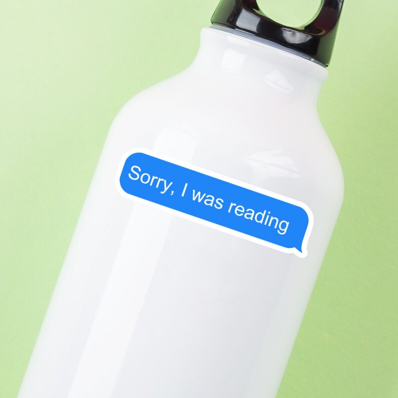 May include: White water bottle with a black cap and handle. A blue speech bubble sticker with the text "Sorry, I was reading" is affixed to the bottle. The background is a light green color.