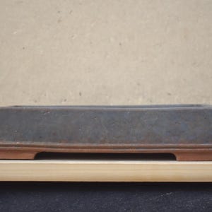 Op de afbeelding: Een rechthoekige bonsai pot met een donkergrijze body en een roodbruine basis. De pot is gemaakt van keramiek en staat op een houten oppervlak. De pot is ongeveer 30 cm lang.