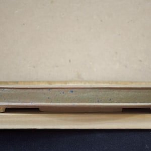 Pode incluir: Um vaso de bonsai oval feito à mão. O vaso de cerâmica tem um esmalte verde claro com manchas azuis e uma borda marrom avermelhada. O vaso mede aproximadamente 30 cm de comprimento e 20 cm de largura, com um perfil baixo e pés retangulares.