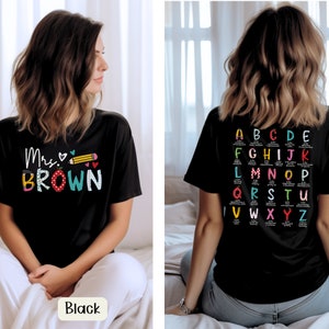 May include: Black t-shirt with the text "Mrs. Brown" and a pencil and hearts design on the front. The back of the shirt has a colorful alphabet chart.