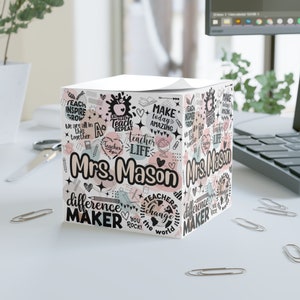 Puede incluir: Un bloc de notas cuadrado blanco con un diseño rosa, verde y negro. El bloc de notas tiene una variedad de frases e ilustraciones con temática de profesores, incluyendo manzanas, corazones y un globo terráqueo. El bloc de notas está personalizado con el nombre "Mrs. Mason".