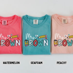 Może przedstawiać: Trzy koszulki Comfort Colors w kolorze arbuza, morskiej piany i brzoskwini. Każda koszulka ma napis "Mrs. Brown" z oł&oacute;wkiem i sercem. Koszulki są w rozmiarze XL-TO-EG.