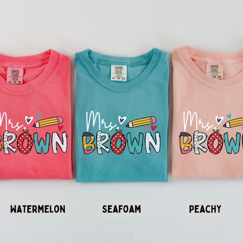 Może przedstawiać: Trzy koszulki Comfort Colors w kolorze arbuza, morskiej piany i brzoskwini. Każda koszulka ma napis "Mrs. Brown" z oł&oacute;wkiem i sercem. Koszulki są w rozmiarze XL-TO-EG.