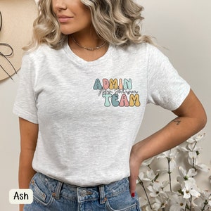 Op de afbeelding: Een grijs T-shirt met een kleurrijke afbeelding waarop "Admin Team" staat, met daaronder de naam "Mrs. Johnson" in cursief.