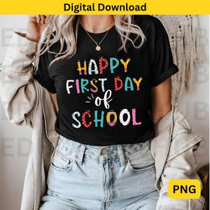 May include: A black t-shirt with the text "Happy First Day of School" in colorful letters with a school-themed design. The letters are decorated with colorful polka dots, pencils, and apples.