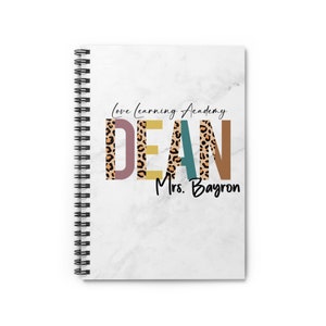 May include: A white marble spiral notebook with the text "Love Learning Academy" and the name "DEAN" in colourful letters with a leopard print pattern. The text "Mrs. Bayron" is below the name.