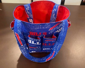 May include: A blue tote bag with red detailing and handles. The bag features the text "BILLS" and a logo design. The interior is red. The bag has multiple pockets on the front. The bag is made of fabric.