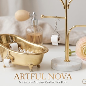 Peut inclure: Une baignoire miniature dorée remplie de perles et deux boucles d'oreilles en rouleau de papier toilette. Un présentoir à bijoux doré présente une seule boucle d'oreille en rouleau de papier toilette. L'image comprend un flacon de parfum et le texte "ARTFUL NOVA".