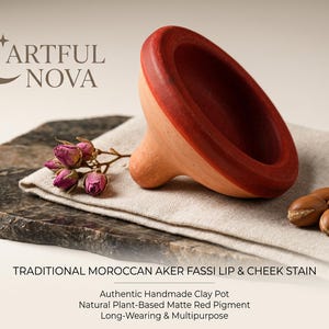 Peut inclure: Un pot en argile fait à la main avec un bord rouge et un corps en argile naturelle, présenté avec des boutons de roses séchées et des noix d'argan. Il s'agit d'une teinture traditionnelle marocaine Aker Fassi pour les lèvres et les joues.