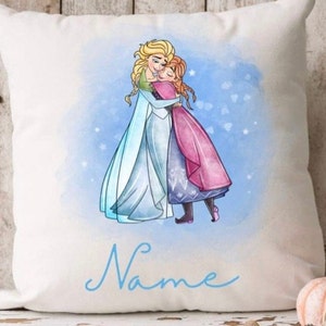 Könnte beinhalten: Ein weißes Kissen mit einer Aquarell-Illustration von zwei Mädchen, die sich umarmen. Die Mädchen tragen blaue und rosa Kleider. Der Text "Name" ist in blauer Kursivschrift am unteren Rand des Kissens geschrieben.