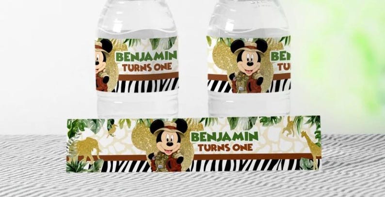 May include: Two water bottles with custom labels featuring Mickey Mouse in safari attire. The labels read "BENJAMIN TURNS ONE" in green text, set against a zebra stripe and jungle-themed background. A matching label is also visible.