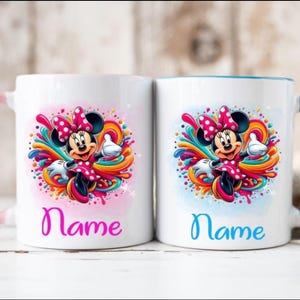 Op de afbeelding: Twee witte keramische mokken met roze en blauwe handvatten. Beide mokken hebben een kleurrijk ontwerp met een cartoonafbeelding van Minnie Mouse. De tekst "Name" is in roze en blauw op elke mok gedrukt.
