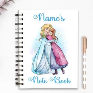 Könnte beinhalten: Ein weißes Notizbuch mit Spiralbindung. Der Einband zeigt eine Aquarell-Illustration von zwei Prinzessinnen aus dem Film Frozen, die sich umarmen. Der Text "Name's Note Book" ist in Blau unter der Illustration gedruckt.