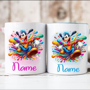 Op de afbeelding: Twee witte keramische mokken met kleurrijke verfspatten ontwerpen. Elke mok heeft een cartoonhond personage met een blauwe en oranje outfit. De mok aan de linkerkant heeft een roze handvat en de tekst "Name" in roze. De mok aan de rechterkant heeft een blauw handvat en de tekst "Name" in blauw.