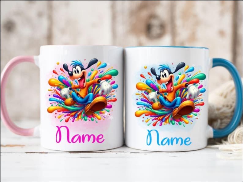 Op de afbeelding: Twee witte keramische mokken met kleurrijke verfspatten ontwerpen. Elke mok heeft een cartoonhond personage met een blauwe en oranje outfit. De mok aan de linkerkant heeft een roze handvat en de tekst "Name" in roze. De mok aan de rechterkant heeft een blauw handvat en de tekst "Name" in blauw.