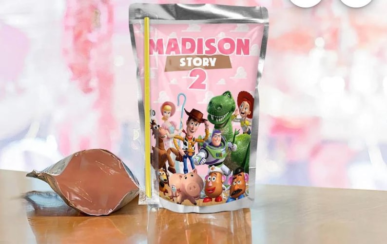 Pu&ograve; includere: Una busta di succo rosa con la scritta "MADISON STORY 2" e una cannuccia gialla. La busta presenta i personaggi del film Toy Story. Una seconda busta parzialmente riempita &egrave; visibile a sinistra.