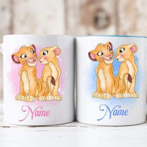 May include: Two white ceramic mugs with pink and blue handles. Each mug features a cartoon image of two lion cubs, one with a pink background and the other with a blue background. The text "Name" is printed on each mug.