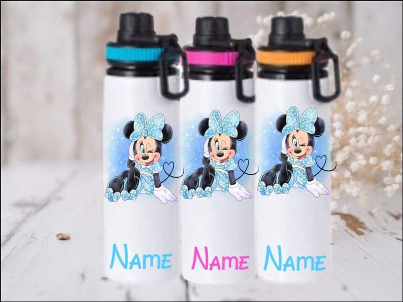 Puede incluir: Tres botellas de agua blancas con tapas negras y detalles coloridos. Cada botella presenta una imagen de dibujos animados de Minnie Mouse con un vestido azul con lunares blancos y un lazo rosa. Las botellas tienen la palabra "NAME" impresa en la parte inferior en diferentes colores.