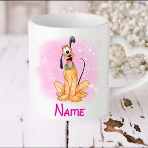 Puede incluir: Taza de cerámica blanca con asa en forma de corazón. La taza presenta una imagen de dibujos animados de Pluto, un personaje de perro de Disney, sobre un fondo rosa con purpurina blanca. El texto "Name" está impreso debajo de la imagen.