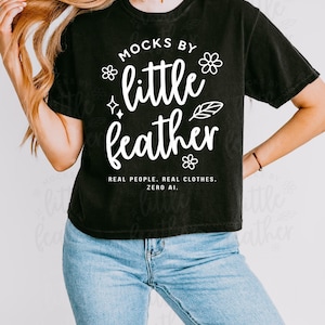 Woman wearing a black comfort colors 3023cl t-shirt with bold white text that says 'Mocks by Little Feather – Real People. Real Clothes. Zero AI.' surrounded by doodle-style flowers and feathers. Trendy Etsy-style mockup featuring real model photography for print-on-demand sellers.