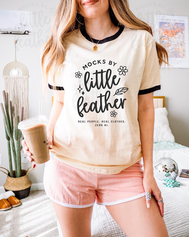 Next Level 3604 unisex ringer t-shirt mockup in natural with black trim, modeled indoors with a casual, boho vibe. The female model is styled in pink lounge shorts and accessorized with silver rings and layered gold jewelry, standing in a bright bedroom with cactus decor, a disco ball, and retro accents. Perfect for showcasing custom print-on-demand designs for Etsy listings, loungewear branding, and vintage-inspired apparel shops.