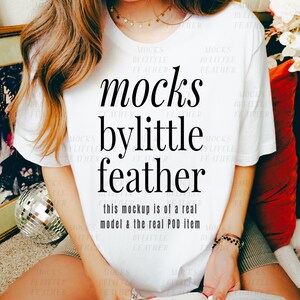 May include: White t-shirt with black text that reads "mocks bylittle feather" and "this mockup is of a real model & the real POD item".