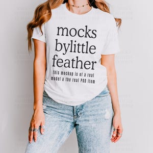 May include: White t-shirt with black text that reads "mocks bylittle feather this mockup is of a real model & the real POD item".