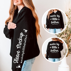 Könnte beinhalten: Ein schwarzes Langarm-Sweatshirt mit weißem Text auf dem Ärmel, der Sleeve Mockup mocksbylittlefeather lautet, sowie Sternsymbolen. Zwei kreisförmige Einsätze zeigen die Vorder- und Rückseite des Sweatshirts mit dem Text mocks by little feather.
