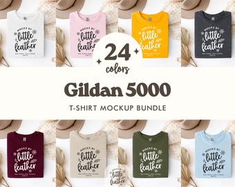 Puede incluir: Un paquete de maquetas de camisetas Gildan 5000 en 24 colores. Cada camiseta doblada muestra el texto "Mocks by Little Feather" en blanco. La imagen incluye sombreros y elementos decorativos, con el texto "T-SHIRT MOCKUP BUNDLE".