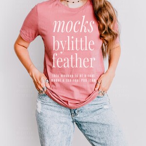 May include: A woman wearing a dusty rose t-shirt with the text "mocks bylittle feather" and the text "this mockup is of a real model & the real POD item" printed on the front. She is wearing blue jeans.